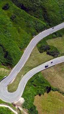 Yukardan görülen viraj yolu, İtalyan dolomitleri dağlarında yeşil bir çayırda giden arabalarla birlikte.