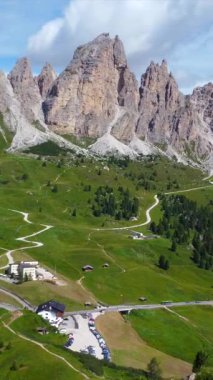 Dolomitlerdeki manzaralı bahçe geçidinin nefes kesen manzarası, dolambaçlı yollar, yeşil vadiler ve parlak mavi gökyüzünün altındaki görkemli zirveler.