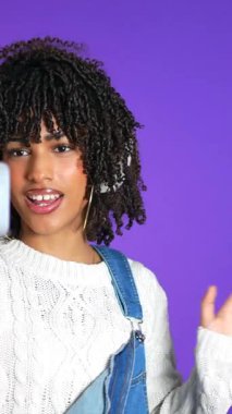 Genç bayan içerik yaratıcısı takipçilerini selamlıyor, akıllı telefon ve mikrofon kullanarak bir video bloğu kaydederken konuşuyor ve işaret ediyor.