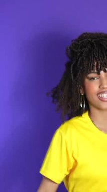 Dinamik genç Afrikalı Amerikalı kadın bulaşıcı bir neşeyle dans ediyor, sarı gömlek ve kot pantolon giyiyor canlı mor stüdyo arkaplanına karşı