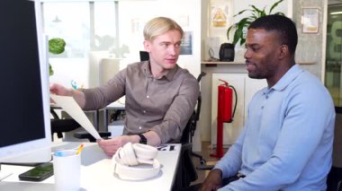 İki işadamı, çağdaş bir ofis ortamında verimli bir konuşma yaparak evrak işlerini birlikte gözden geçirir.