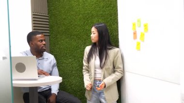 Asyalı iş kadını, modern çalışma ofisindeki Afrikalı Amerikalı iş adamına proje stratejisini anlatıyor