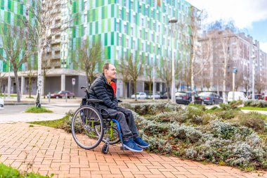 Engelli adam tekerlekli sandalyesinde oturuyor, şehir ortamının tadını çıkarıyor ve şehir manzarasını inceliyor.