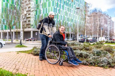 Bakıcı tekerlekli sandalyedeki mutlu engelli bir adama yardım ediyor, birlikte şehir gezintisinden zevk alıyor, ulaşılabilirliği ve dahil edilmeyi teşvik ediyor.