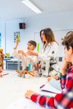 Güvenlik gözlüğü ve laboratuvar önlüğü takan öğrenciler modern bir laboratuarda deney tüpleri ve deney tüpleriyle kimya deneyi yapıyorlar.