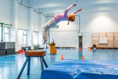 Jimnastik yapan bir kız, okul spor salonunda atlayan bir atın üzerinden atlamak, atletizm ve kendini spora adamak.