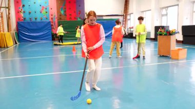 İlkokul öğrencileri beden eğitimi dersinde florbol oynuyorlar, takım çalışması ve sportmenlik yapıyorlar.