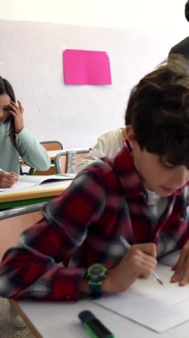 Öğrenci, okuldaki eğitim dersi sırasında not defterine yazarken konsantre oluyor, derslik ortamında odaklanmış öğrenme anını yakalıyor.