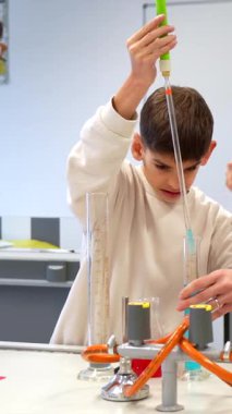 Kimya öğretmeni genç bir öğrenciye okul laboratuarında renkli sıvılarla ilgili bir deney yapması için yardım ediyor.