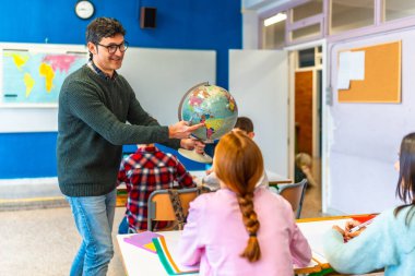 Coğrafya öğretmeni coğrafya dersi sırasında dünya üzerindeki bir sınıf dolusu ilkokul öğrencisini işaret ediyor.