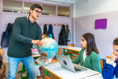 Sınıftaki özenli öğrencilere dünyayı gösteren coğrafya öğretmeni, öğrenme için dizüstü bilgisayar ve geleneksel araçlar kullanıyor