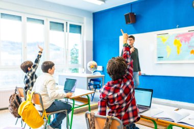 Bir grup ilkokul öğrencisi coğrafya dersinde öğretmenin sorusuna cevap vermek için el kaldırıyor.