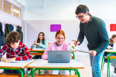 Öğretmen sınıfta gülümseyen bir öğrenciye ders, eğitim ve öğrenim konsepti sırasında dizüstü bilgisayar kullanarak yardım ediyor.