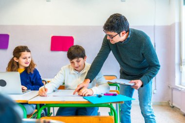 Sınıfta öğrencilere yardımcı olan, kavramları açıklayan ve alıştırmaları düzelten öğretmen, destekleyici bir öğrenme ortamı oluşturmaktadır.