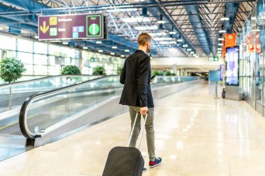 İş adamı tramvayı çekiyor ve havaalanında yürürken akıllı telefon kullanıyor, dijital ekranda geçit bilgilerini kontrol ediyor