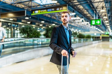 Genç işadamı havaalanı terminalinde yürürken elinde akıllı telefon ve tramvay tutuyor.
