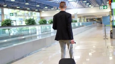 Modern havaalanı terminali koridorunda modern mimari tasarım ile yürürken kendine güvenen profesyonel işadamı bavulu çekiyor.
