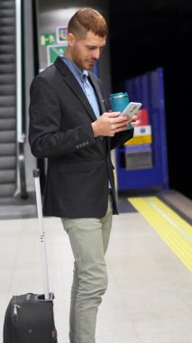Profesyonel işadamı metro istasyonunda duruyor, sabah işe giderken akıllı telefonları kontrol ederken yeniden kullanılabilir bardaktan yudumluyor.