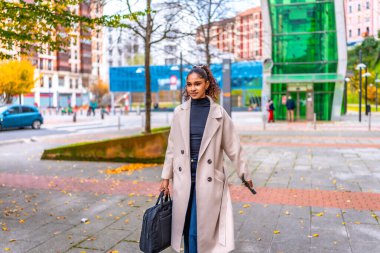 Şehirde dizüstü bilgisayar çantası ve cep telefonu taşıyan Afro-Amerikan genç iş kadını