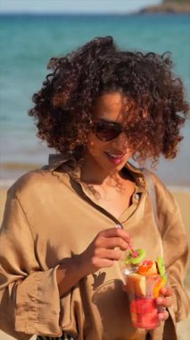 Sahilde tropikal meyvelerle ferahlatan Arap bir kadının dikey yakın plan fotoğrafı.