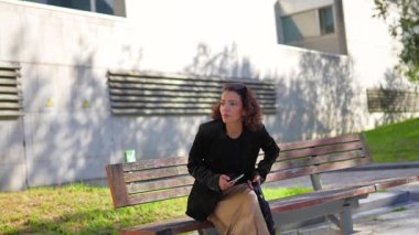 Genç Arap iş kadını konut alanı boyunca dizüstü bilgisayar çantasıyla yürüyor ve cep telefonu kullanıyor.