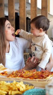Çocukla ilgilenmek, annenle pizza dilimlerini paylaşmak, aile yemeği sırasında aydınlık mutfağın içinde iç açıcı bir bağlantı anı yaratmak.