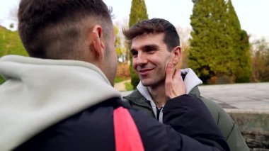 Sevecen eşcinsel çift parkta romantik bir günün tadını çıkarıyor. Birbirlerine sevgi dolu bakışlar, okşamalar ve öpücükler atıyorlar.