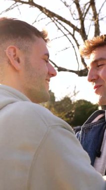 Sevecen eşcinsel çift parkta birbirlerine sevgi dolu bakışlar ve öpücükler atıyor, ilişkilerini kutluyorlar.