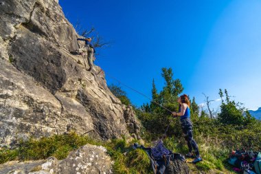 Doğayla çevrili güneşli bir günün tadını çıkaran iki kadın dağcı zorlu bir kaya yüzeyine tırmanıyor.