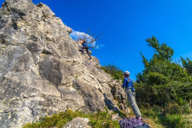 İki kadın dağcı dik bir kaya yüzeyine tırmanıyor, doğada güneşli bir günün tadını çıkarırken maceranın heyecanını kucaklıyorlar.