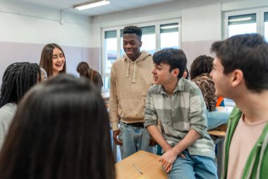 Lise öğrencilerinden oluşan çok ırklı bir grup, sınıf içinde bir okul projesinde işbirliği yaparken takım çalışmasından keyif alıyor.