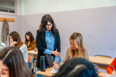 Üniversite profesörü, bir sınavda öğrenciye yardımcı olarak, bir sınıf ortamında destek ve rehberlik sağlamaktadır.