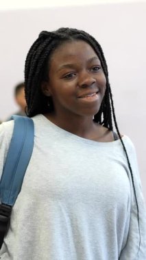 Mutlu Afrikalı Amerikalı öğrenci sırt çantası takıyor, kendine güvenerek duruyor ve temiz beyaz arka planda okul portresi için poz verirken gülümsüyor.