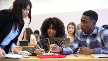 Üniversite profesörü iki öğrenciye bir sınıf ortamında yardım ediyor, projelerinde rehberlik ve destek sağlıyor.
