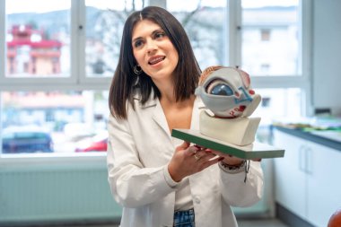 Anatomik göz ve optik sinir modeli taşıyan laboratuvar önlüğü giyen genç bir kadın üniversite sınıfındaki işlevini açıklıyor.
