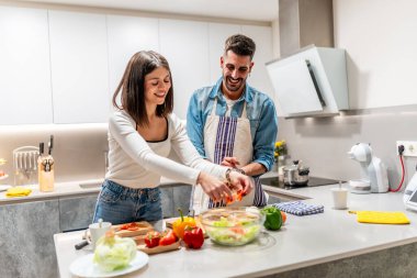 Neşeli çift gülümsüyor ve modern bir mutfakta birlikte sağlıklı bir salata hazırlıyor, kaliteli vakit geçiriyorlar.