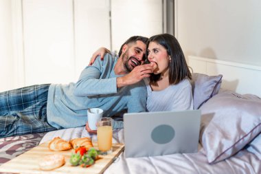 Genç çift yatakta uzanıyor, kahvaltı yapıyor ve bilgisayar başında film izliyor, birlikte vakit geçiriyorlar.