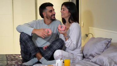 Sevgi dolu partnerler, samimi sabah anının tadını çıkarırlar, yatakta tatlı kahvaltıyı neşeli çöreklerle ve sıcak bir bağlantıyla paylaşırlar.