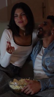 Genç çift samimi film anlarını paylaşıyor, oturma odasındaki kanepede uzanıp evde romantik bir akşam boyunca patlamış mısırın tadını çıkarıyorlar.