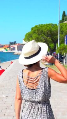 Hasır şapka takan genç bir kadın, yaz tatilinde, Piran gezinti alanında yürüyor, Adriyatik kıyılarının manzarasının keyfini çıkarıyor.
