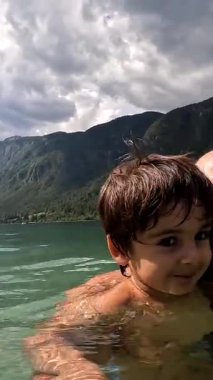 Baba ve oğul, Bohinj gölünün ferahlatıcı sularında birlikte yüzmekten zevk alırken gülümsüyorlar.