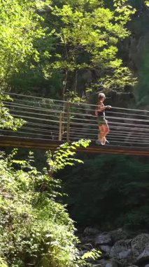 Anne ve çocuk, yaz tatillerinde Triglav Ulusal Parkı 'ndaki Tolmin Vadisi üzerindeki askıya alınmış ahşap köprüde yürüyor.