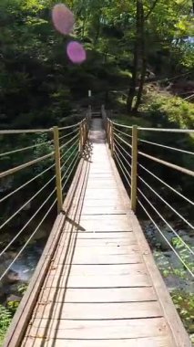 Güneşli bir yaz gününde yemyeşil yeşilliklerle çevrili Tolmin Vadisi, Slovenia 'daki berrak bir dereden tahta asma köprüsü geçiyor.
