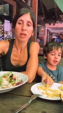 Anne ve oğlu deniz kenarındaki bir restoranda öğle yemeği yiyorlar. Birlikte yaz tatilinin tadını çıkarıyorlar.