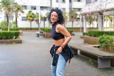 Kıvırcık saçlı dansçı şehir parkında modern dans hareketleri yapıyor, özgürlük ve hareketin tadını çıkarıyor.