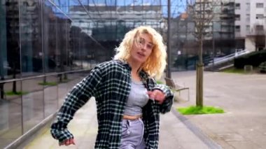 Enerjik genç kadın, dinamik hareketler ve neşeli ifadelerle kendini ifade ederek şehir ortamında özgürce dans ediyor.