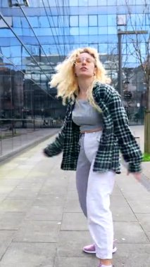 Enerjik genç bir kadın modern bir şehir ortamında özgürce dans ediyor, hareketlerini cam binaların önünde sergiliyor.