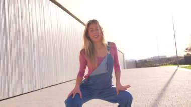 Sarışın kadın modern binanın yakınında enerjik şehir dansı hareketleri sergiliyor. Serbest stil koreografisini dinamik hareket ve tutkuyla ifade ediyor.