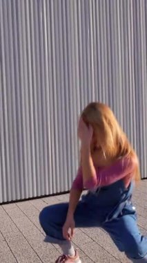 Modern metalik bir duvarın önünde dans figürleri sergileyen enerjik sarışın dansçı.