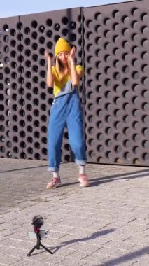 Enerjik sarışın dansçı şehir dansı hareketleri sergiliyor, kendini akıllı telefon ve harici mikrofonla kaydediyor.